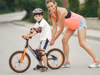 Mother helping her son ride a bicycle in a sunny outdoor setting. Bonding and learning experience.